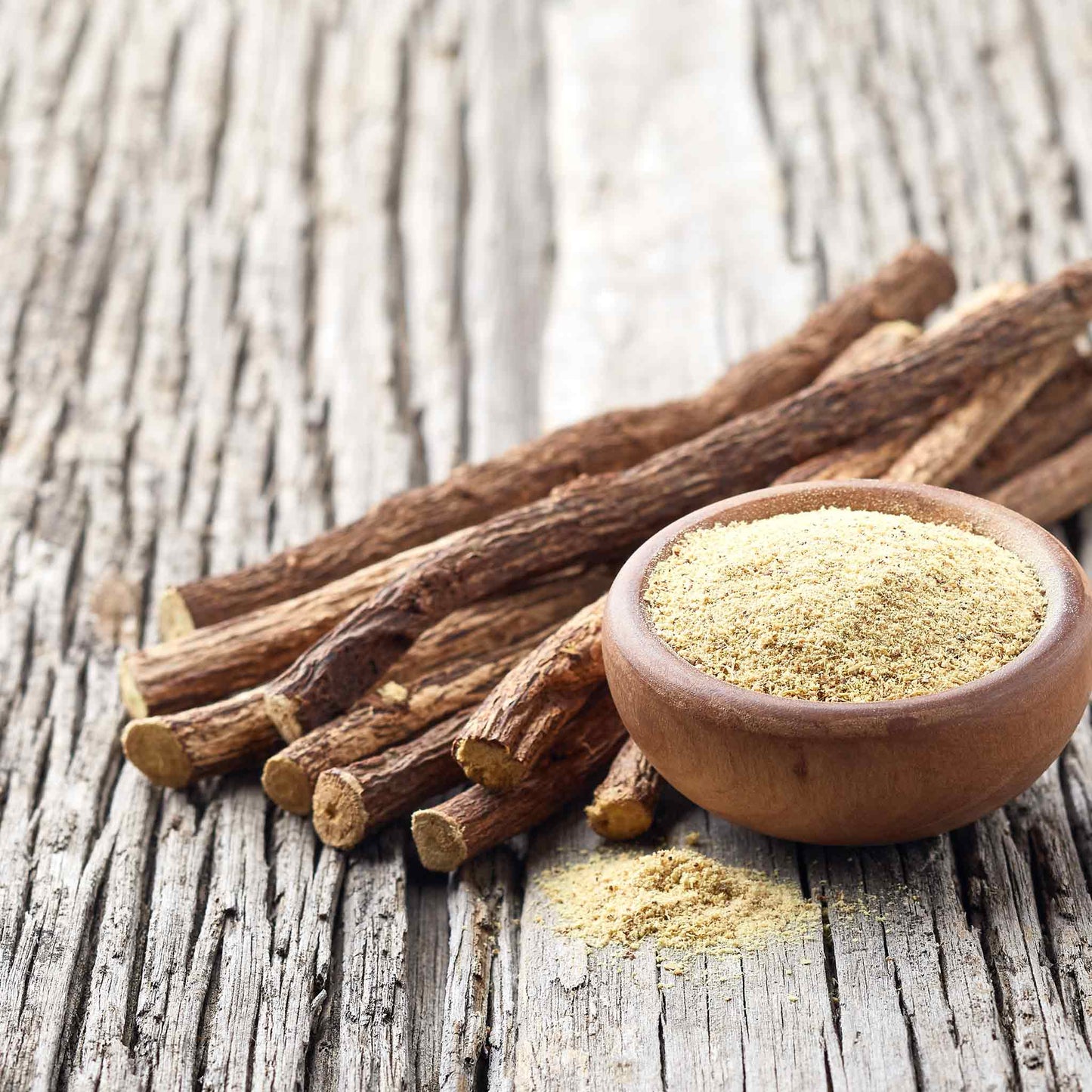 Close-up of three dried licorice roots with textured, brown skin on a light background.