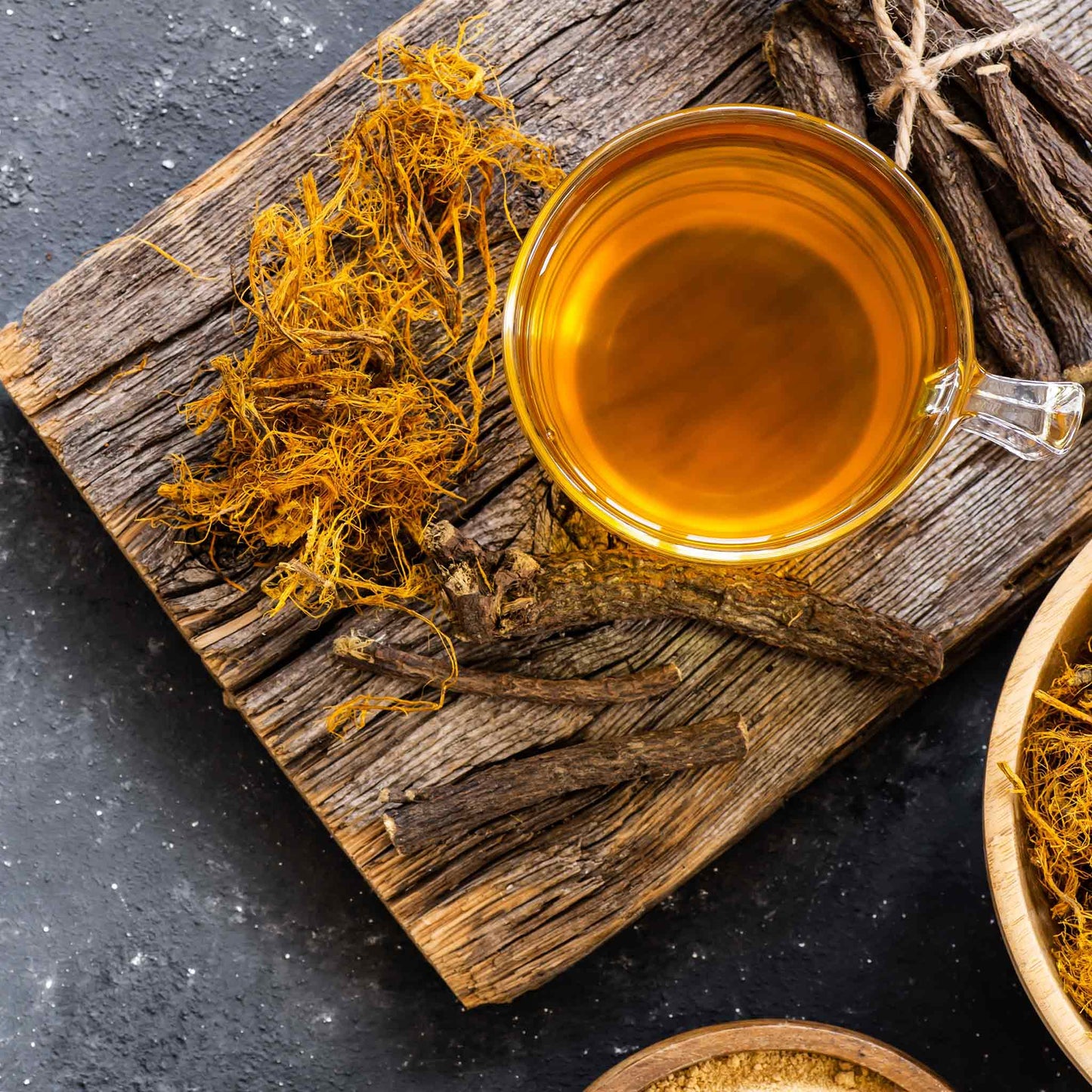 Sprigs of dried licorice root next to licorice tea and dried yellow flowers.