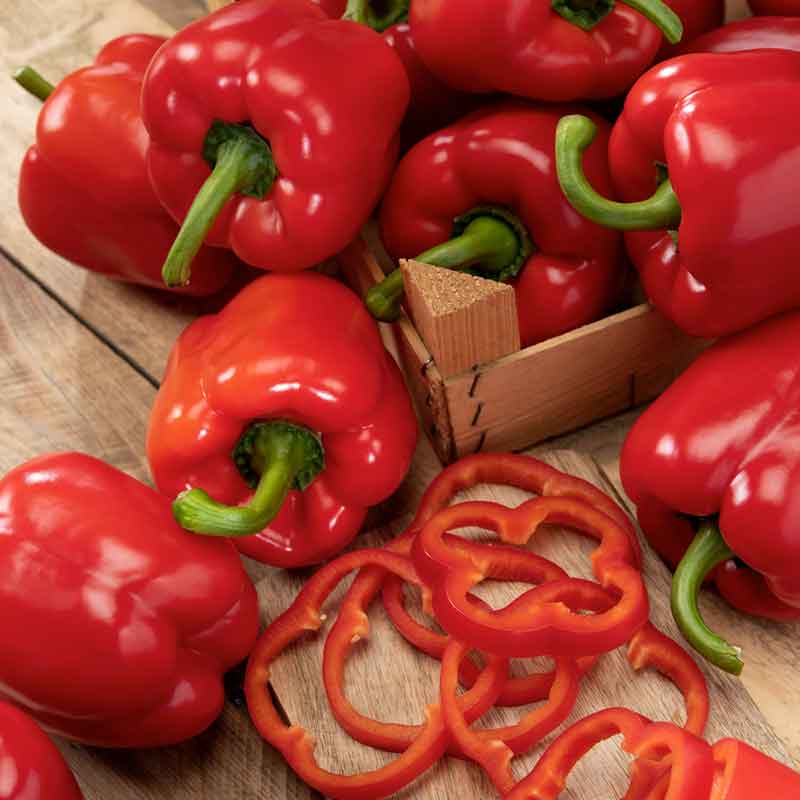 A lot of Big Red Bell peppers showing glossy skin, green stems, and slices of pepper. | copyright: Floramedia UK Ltd