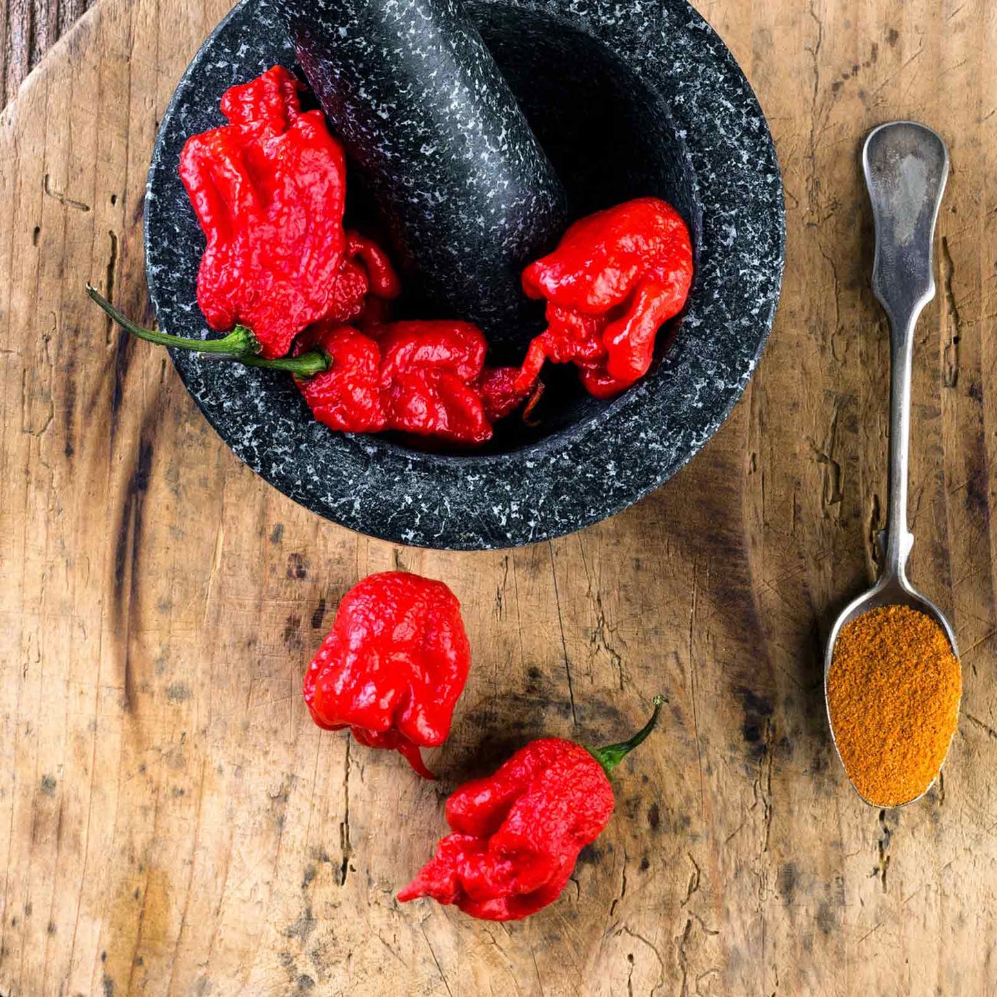 A vivid red Carolina Reaper pepper, known for its extreme heat, is shown close-up.