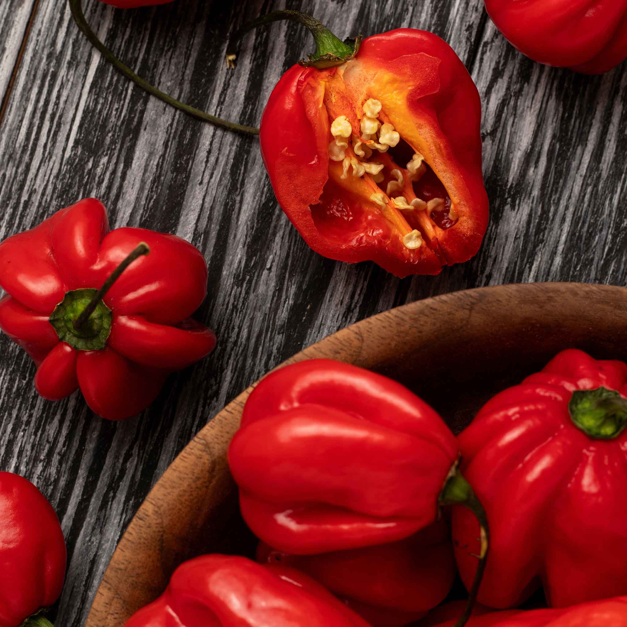 A cluster of shiny, bright red habanero red peppers in a bowl and halved showing its seeds.