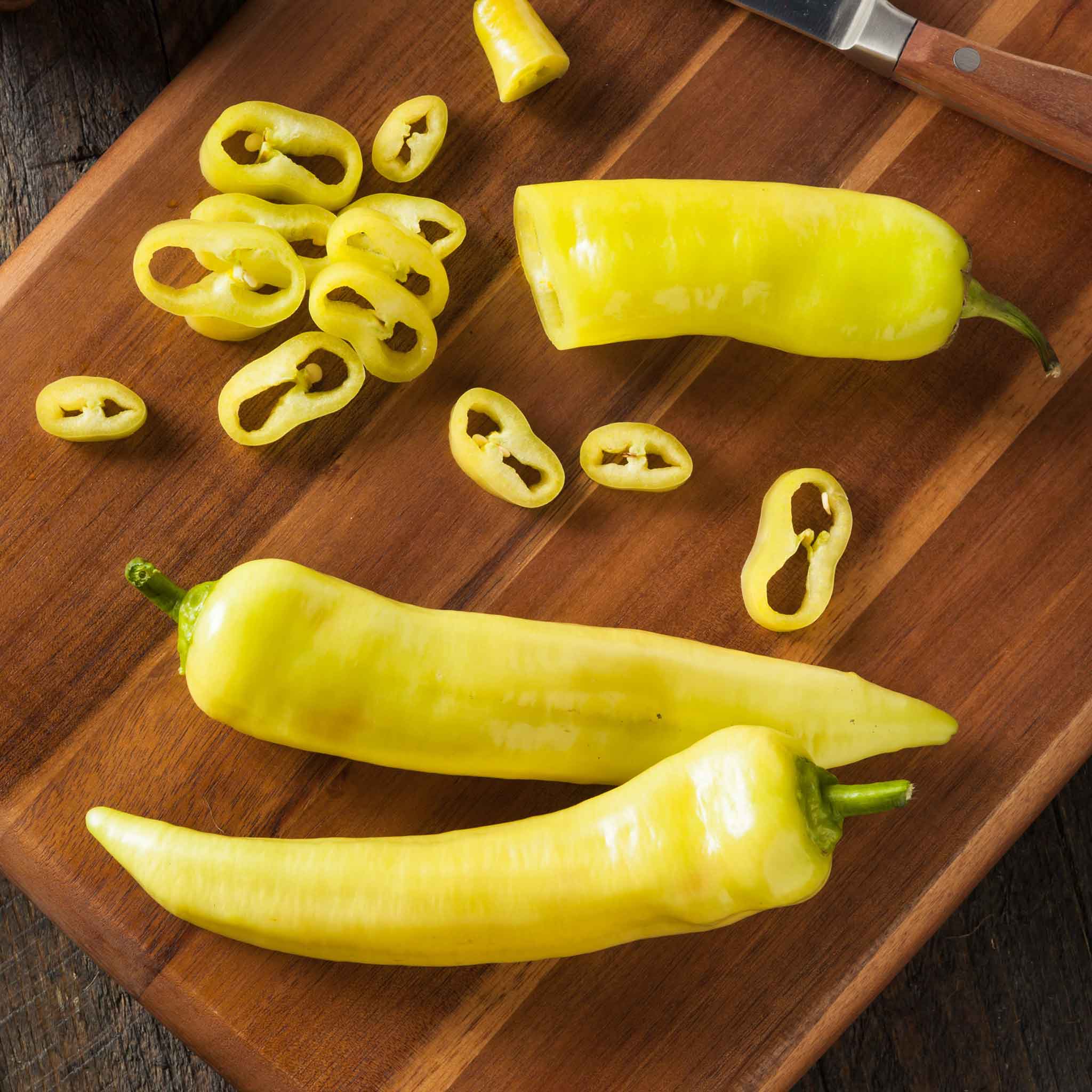 Close-up of a Hungarian Yellow Hot Wax pepper plant with sliced peppers on the board next to it.