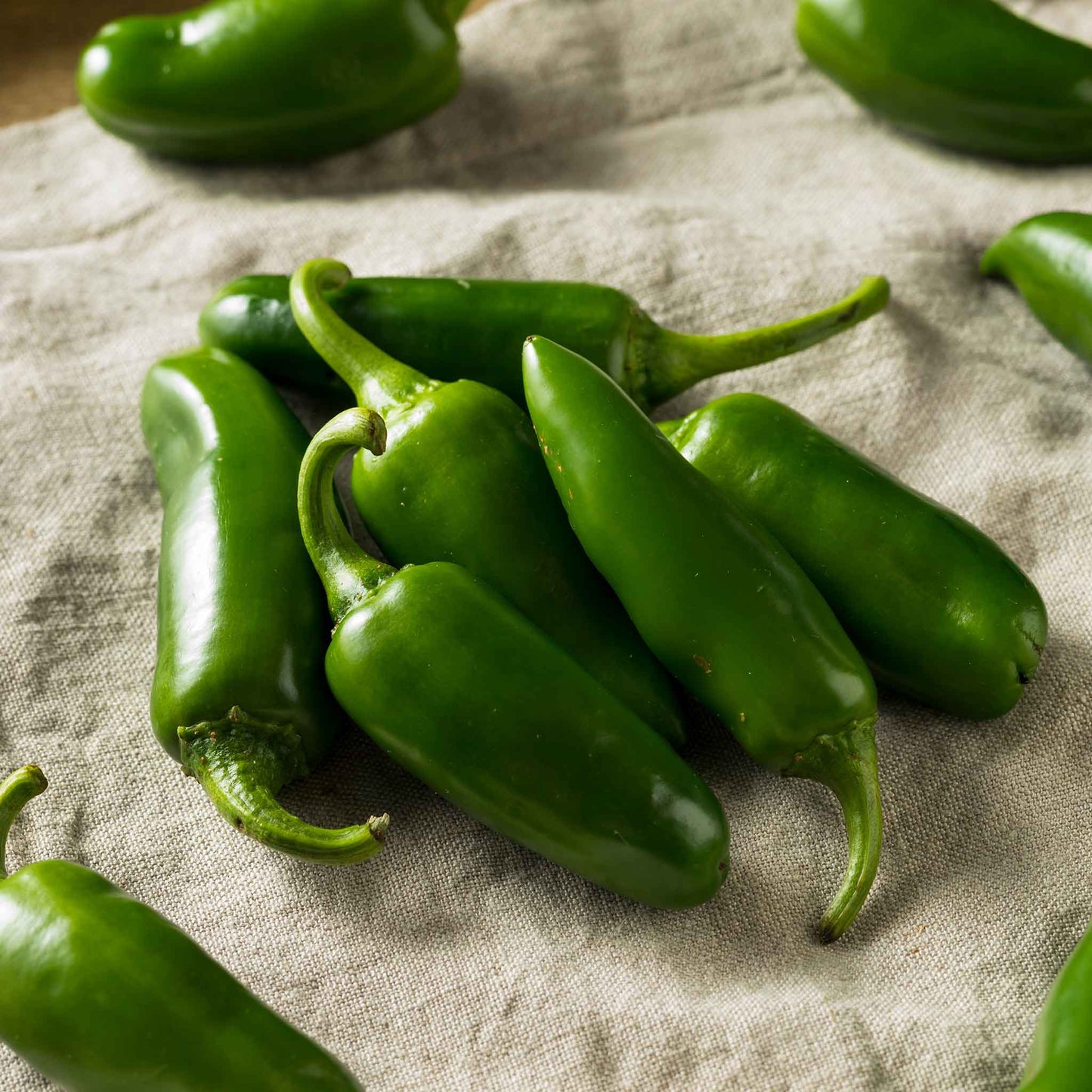 Several bright green Jalapeno Tam peppers are shown in a pile,