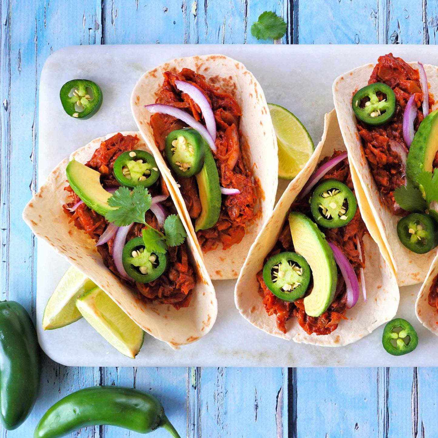 Tacos displayed on a board on top of a wooden surface using Jalapeno Tam peppers.