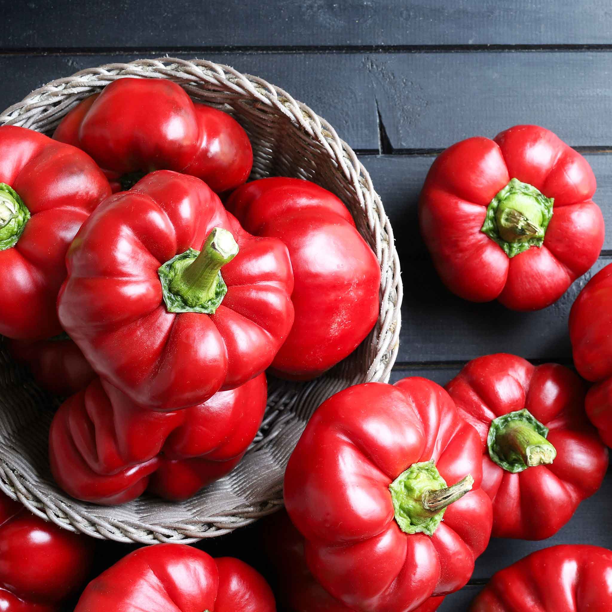 A bowl spilling over with red Pimento peppers with green stems.