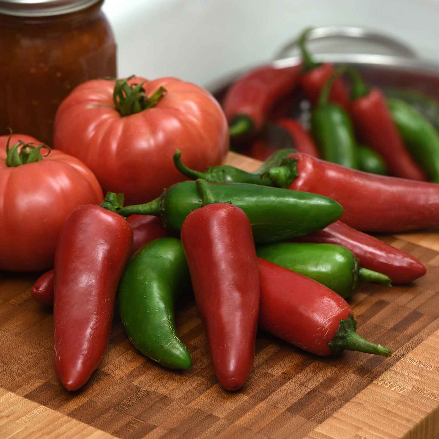 Red and green Pot-a-Peno peppers on a cutting board in front of a tomato.