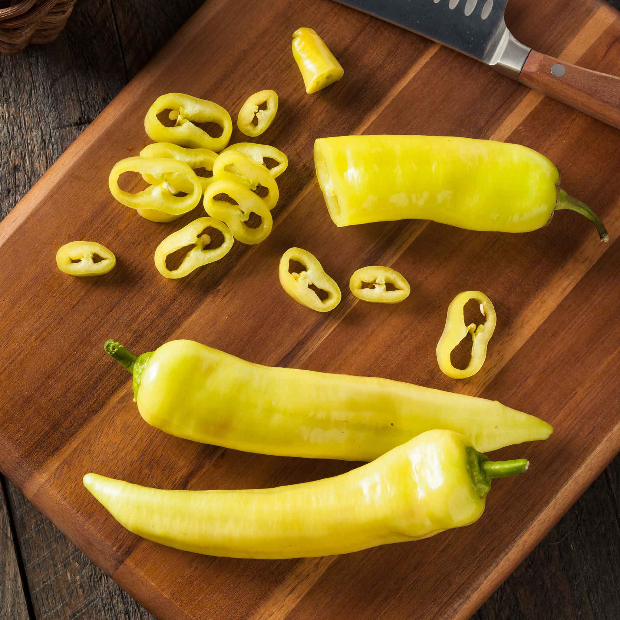 Three ripe yellow Sweet Banana peppers, long and slightly curved, with one sliced ready for cooking.