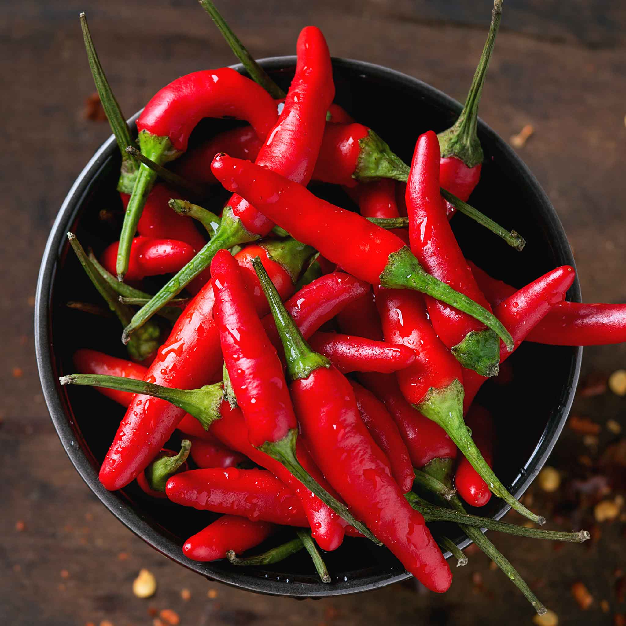A cluster of small, vibrant Thai Super Chili F1 peppers with green stems, in a bowl.