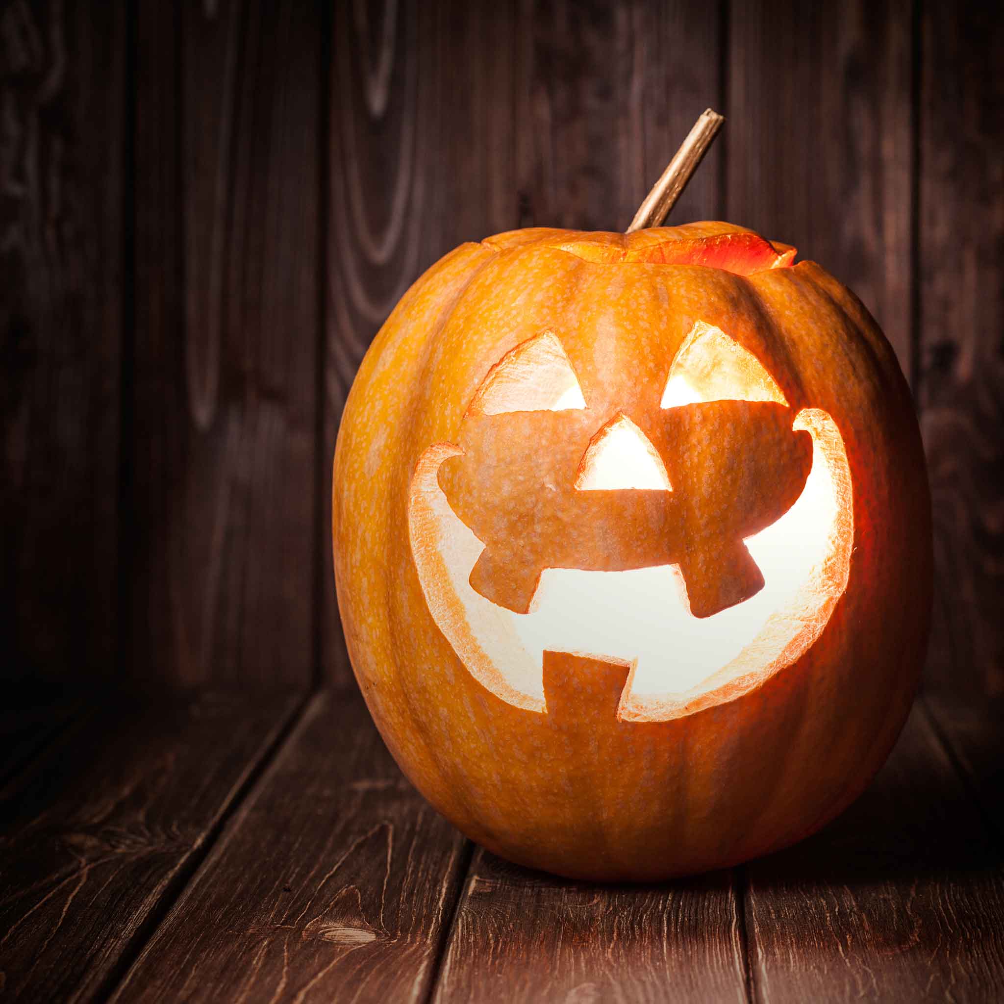 A carved Jack O'Lantern pumpkin with a toothy grin, glowing from within on a dark background.