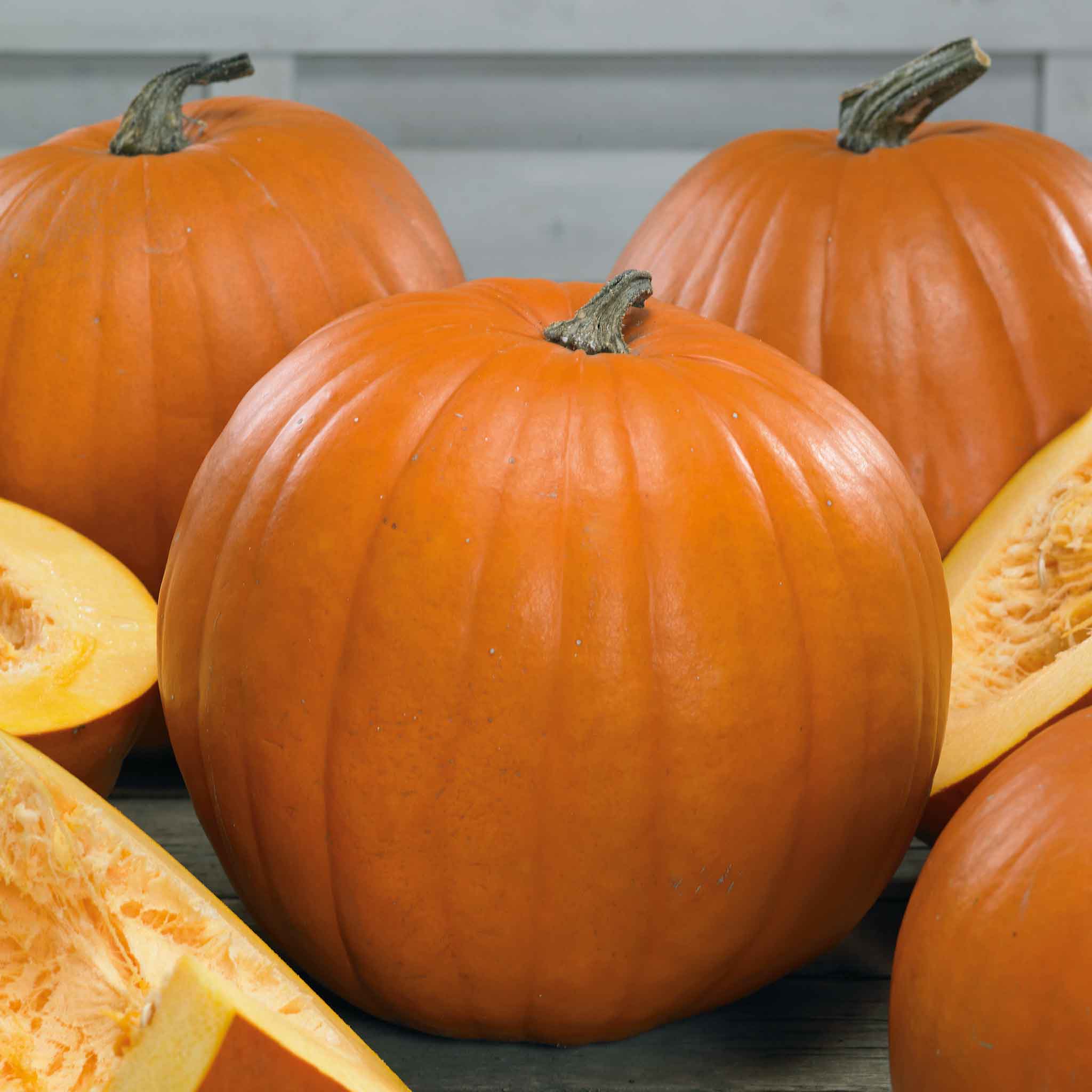 A group of orange Young's Beauty pumpkins with green stems and some cut up.