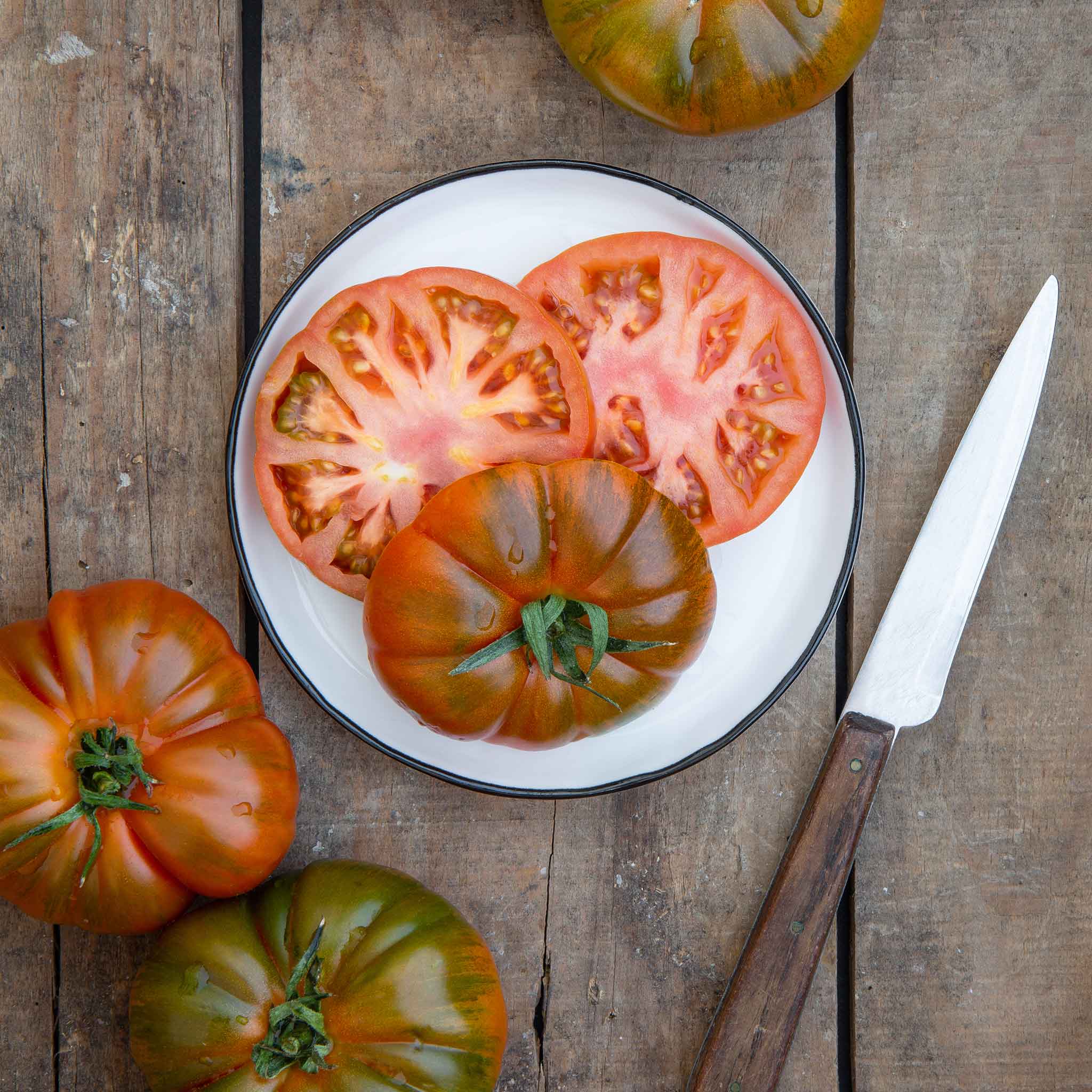 Slices of Black Brandywine tomato with hints of green and brown on its skin, shown on a plate.
