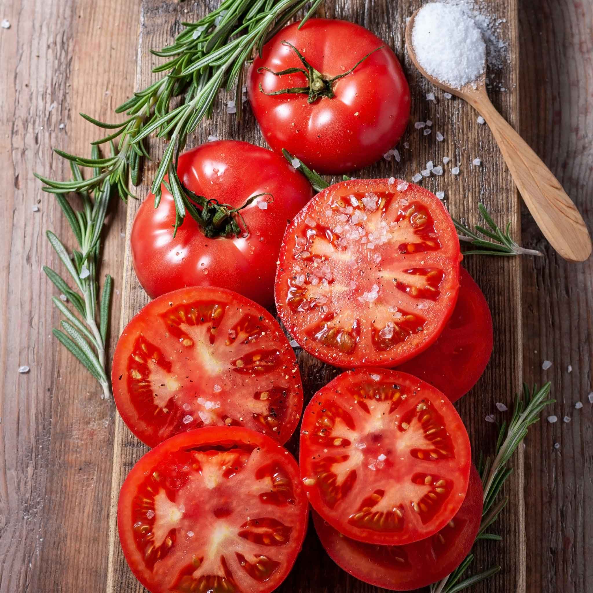 A Burpee's Big Boy tomato sliced and whole on a wooden board.