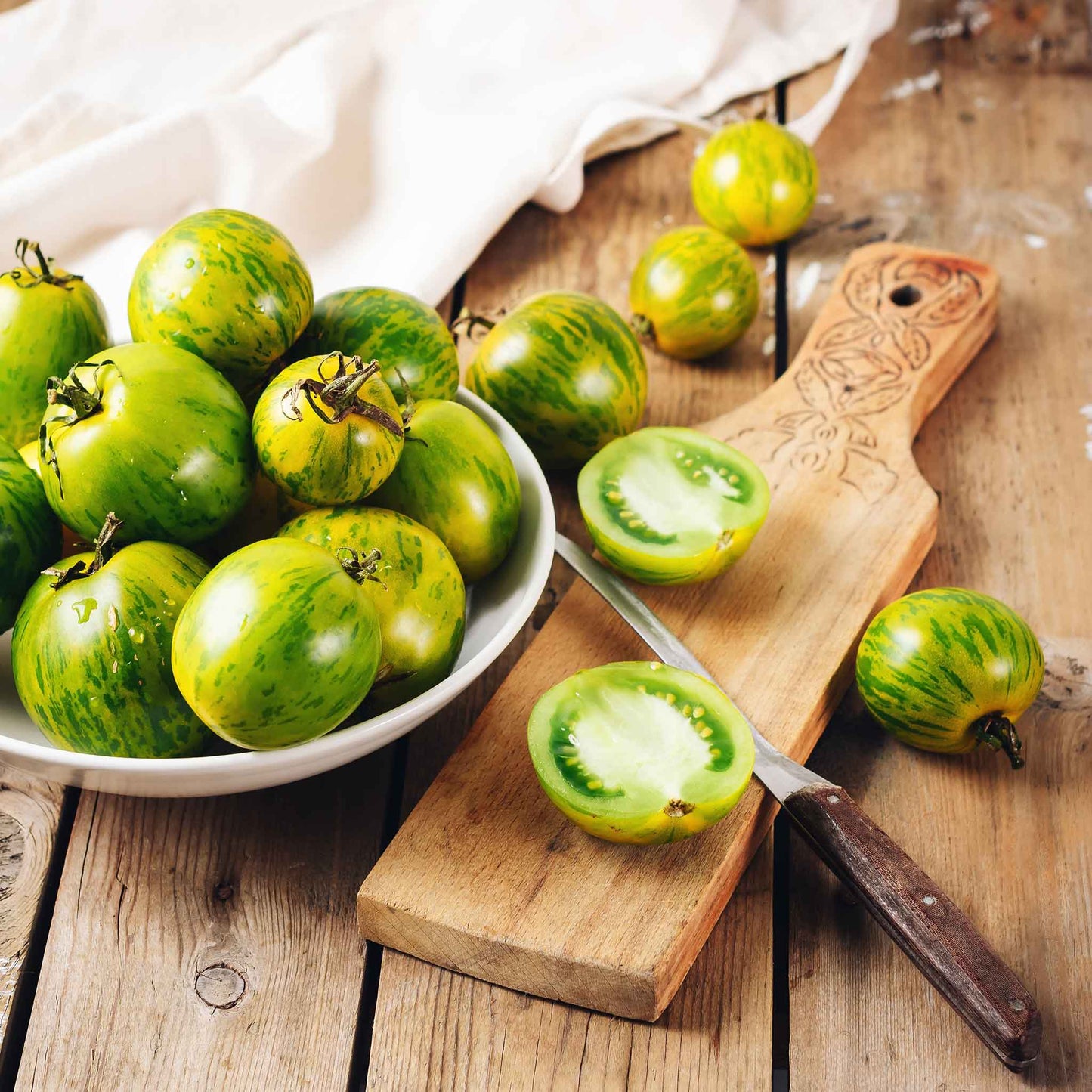 A bowl of Green Zebra tomatoes with sliced tomatoes on a cutting board.