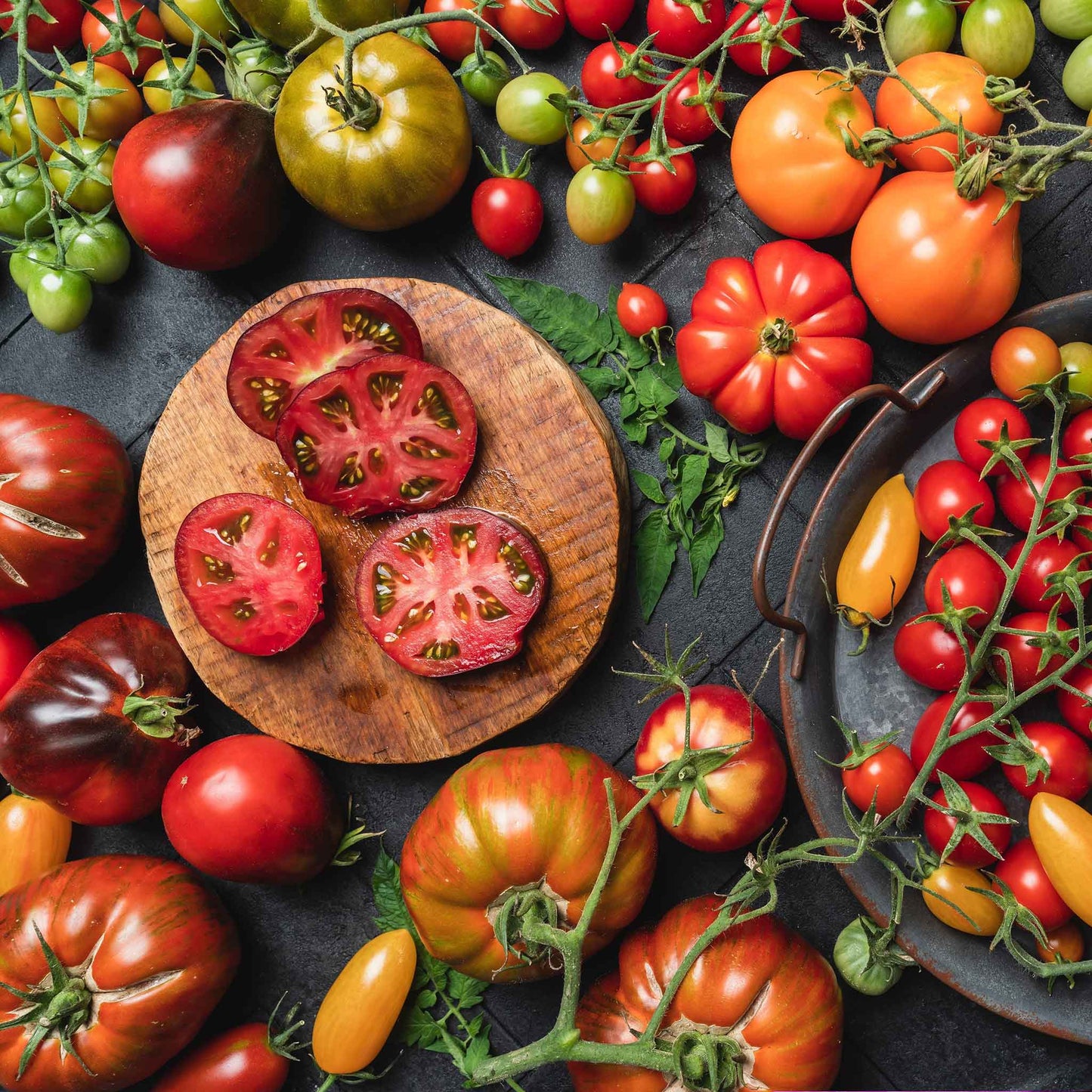 A variety of colorful heirloom tomatoes, including red, yellow, and striped, are displayed on a wooden surface.