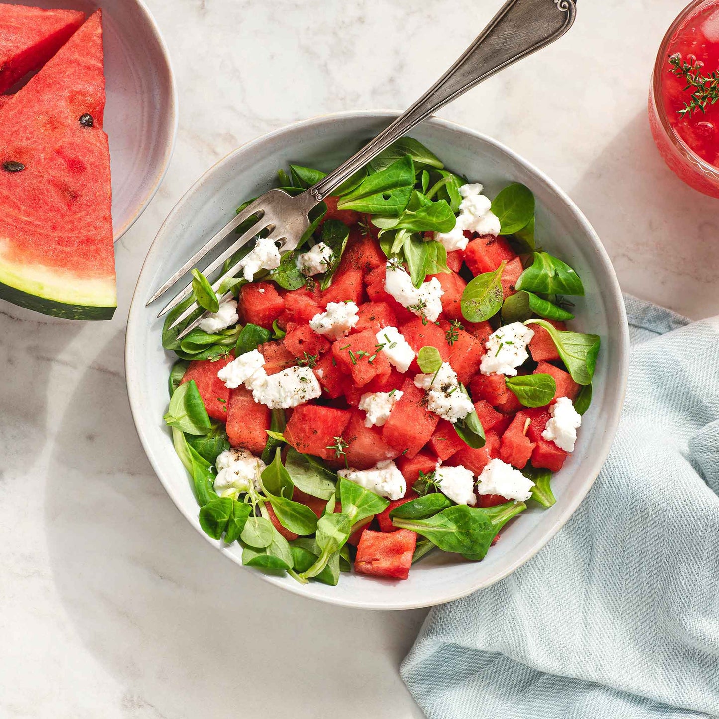 A bowl of watermelon salad with greens, cheese, and watermelon.