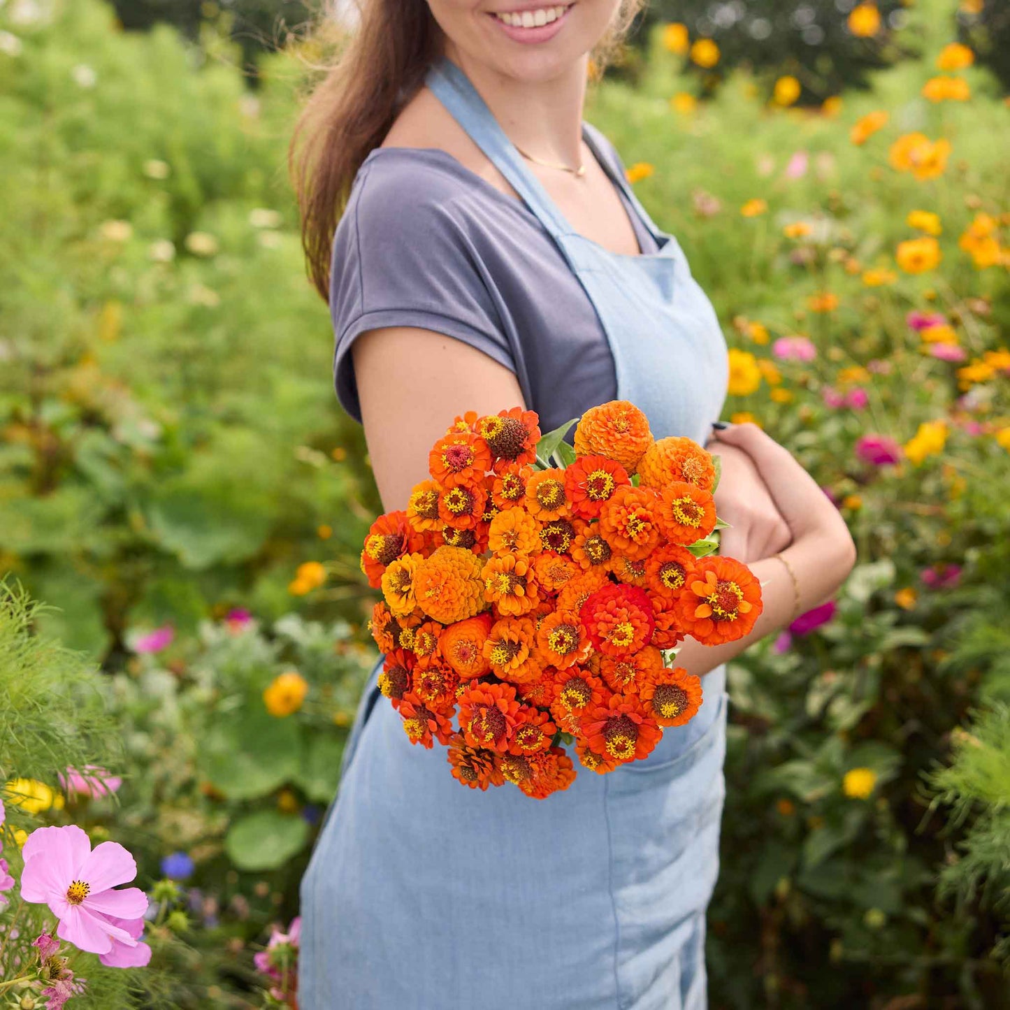 Person holding a bouquet of lilliput orange zinnia flowers in a garden setting