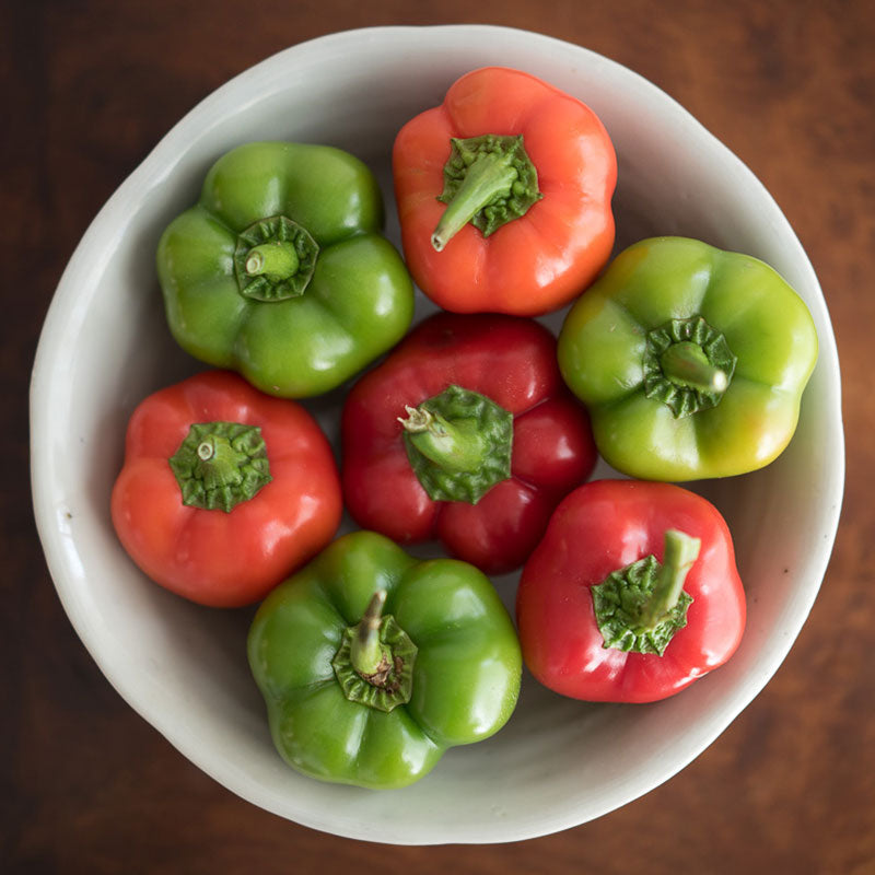 A bowl of red and green Chili Pie F1 peppers with green stems shown from the top.