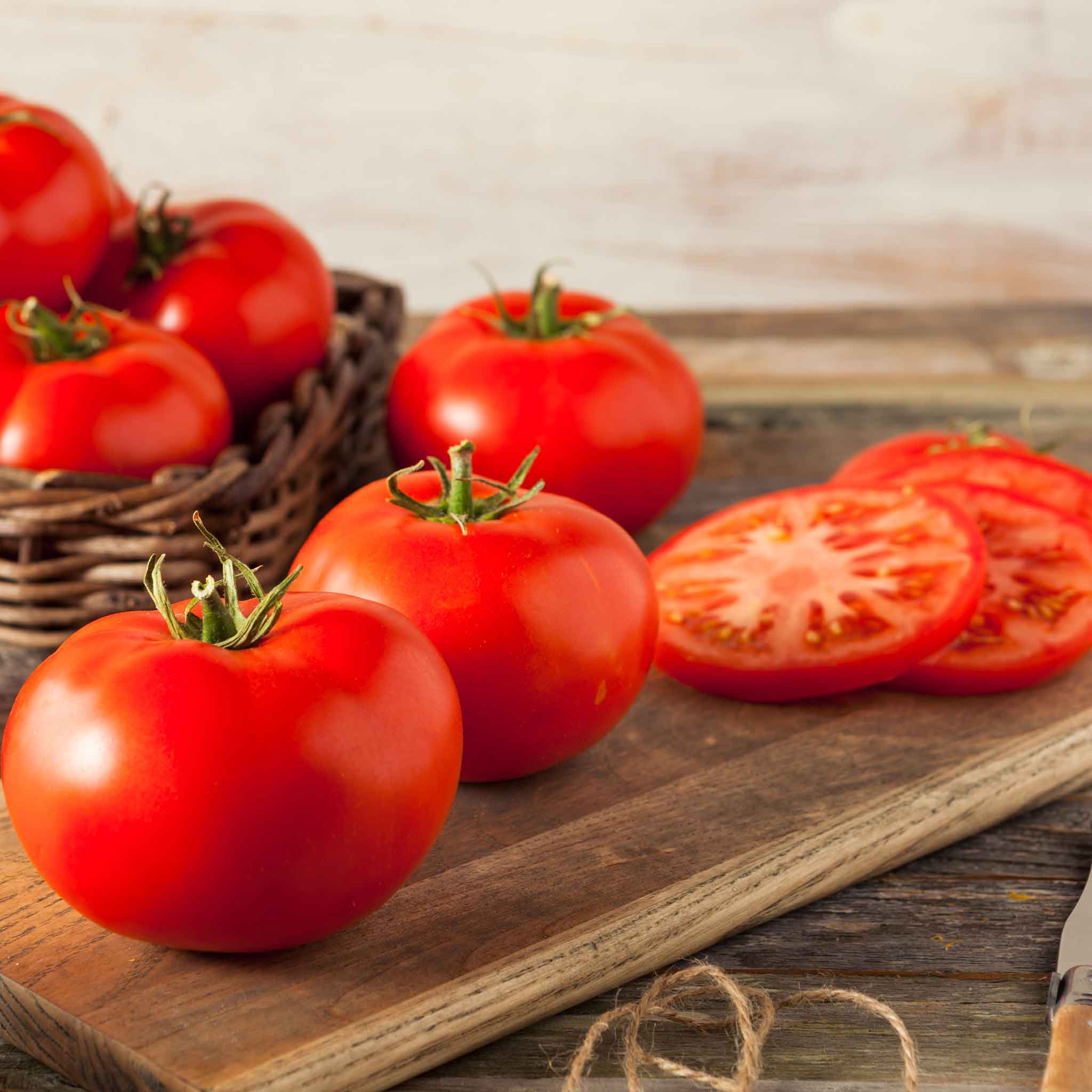 Ripe Beefmaster tomatoes on a board, with with sliced tomatoes in the background.