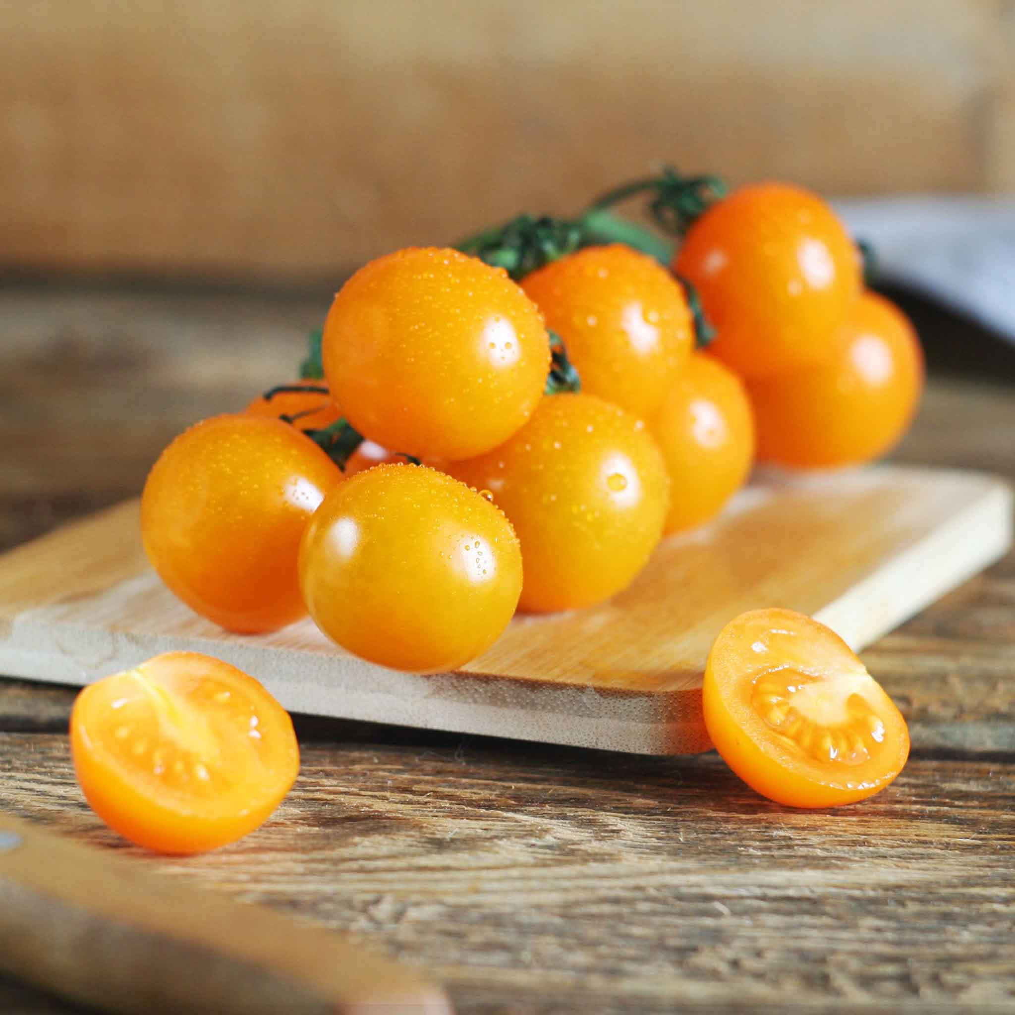 A cluster of ripe, orange Sungold cherry tomatoes on a cutting board.