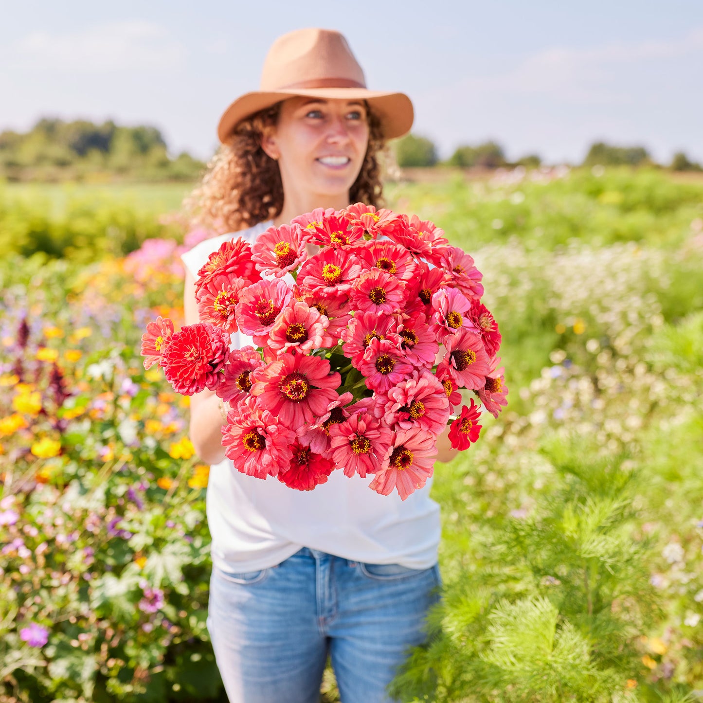 Person holding a bouquet of salmon queen zinnia flowers in a garden setting