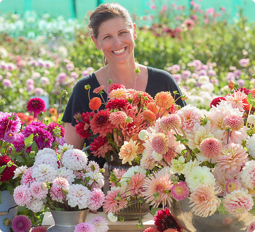 Sabine holding a large bouquet of colorful dahlias in a field with more dahlias in the background.
