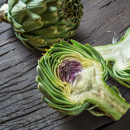 A close-up of a green globe artichoke cut open to show the purple heart of the artichoke.
