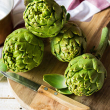 Artichoke tavor heads displayed on a cutting board showing their overlapping green scales.