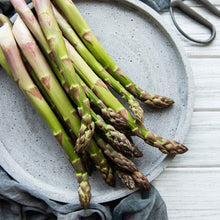 A close-up shot of several bright green asparagus spears with purple tips on a plate.