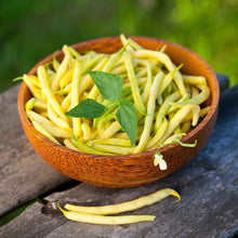 A wooden bowl of yellow Golden Wax beans topped with a leaf.