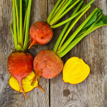 A group of golden detroit beets with green stems and orange-red beetroots showing the bright golden interior on a wooden table.