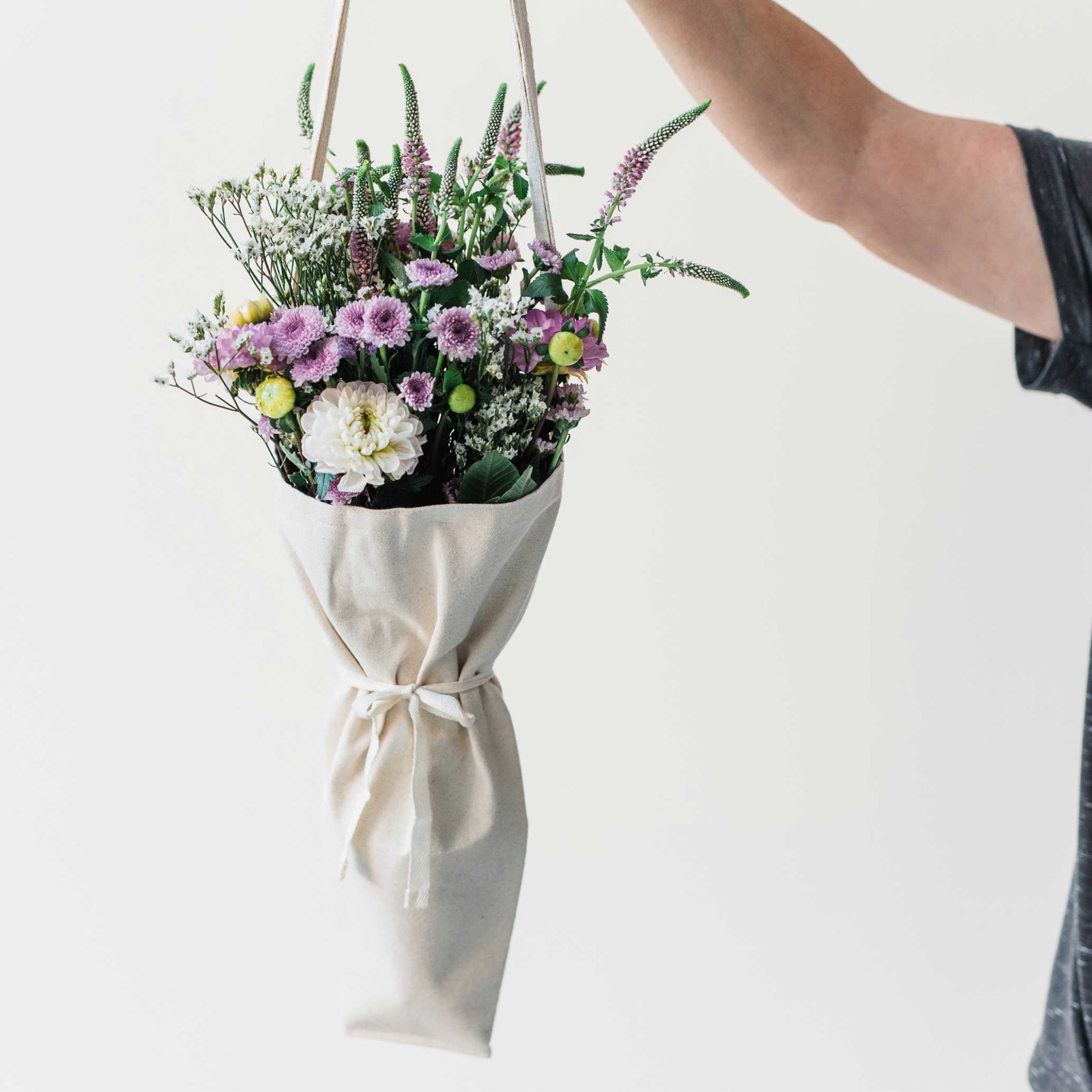 Person holding a bouquet of flowers using the bouqbags gifting tote on a white background