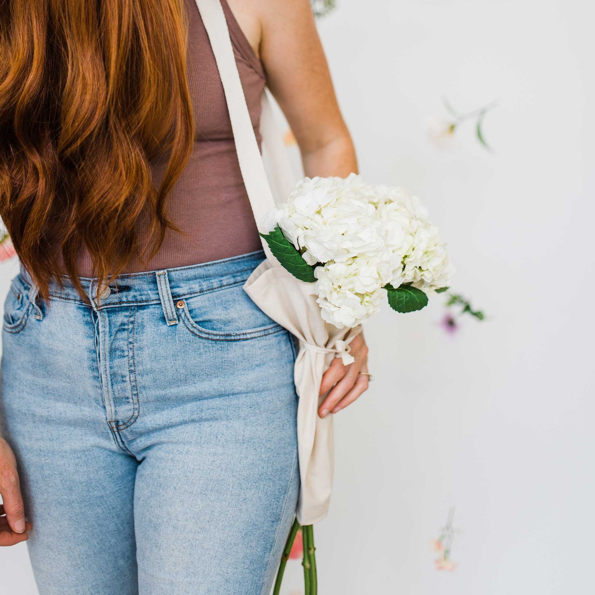 Person holding a bouquet of flowers using the bouqbags gifting tote on a white background