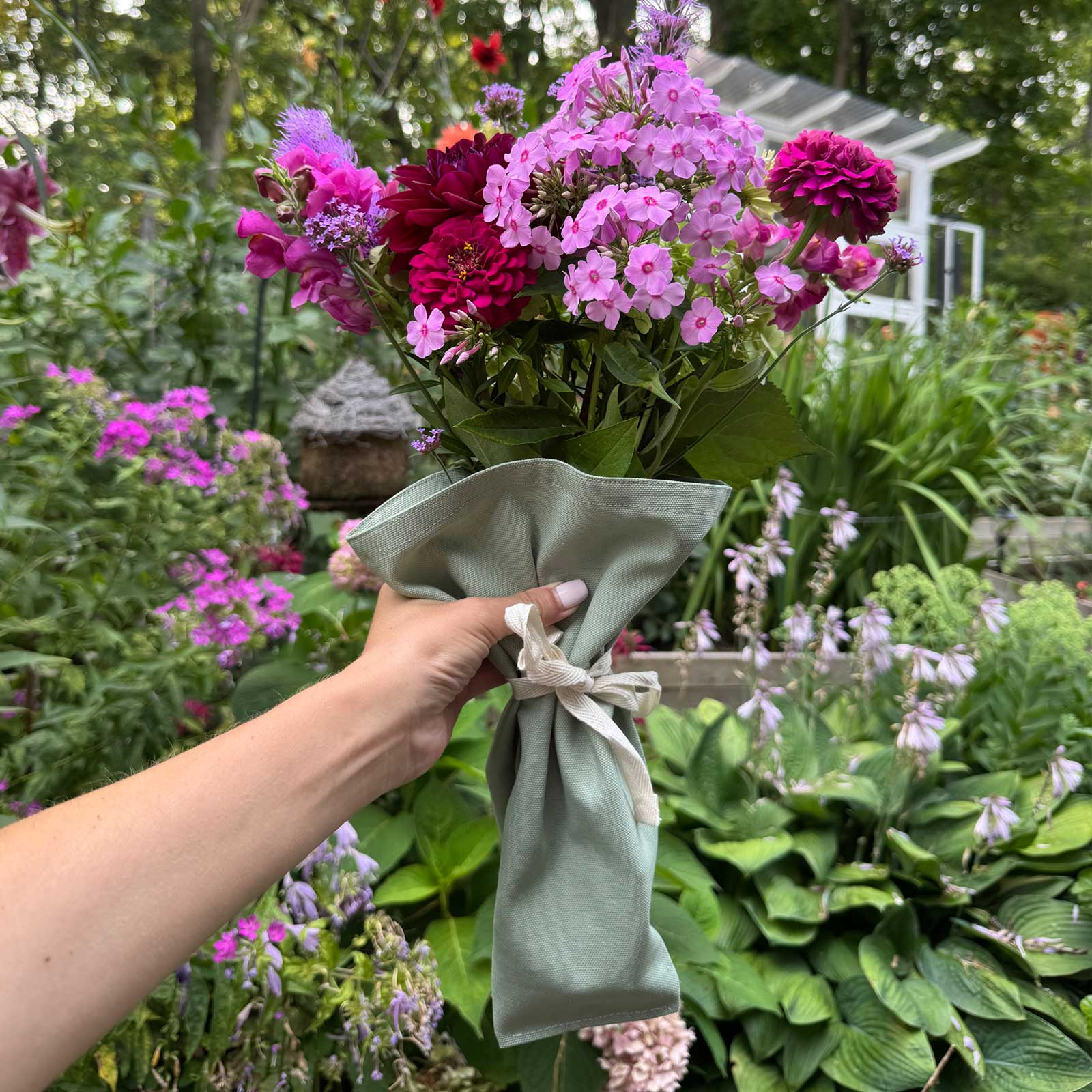 Green Bouqbags natural canvas bouquet sleeves shown holding a bouquet of pink and red flowers
