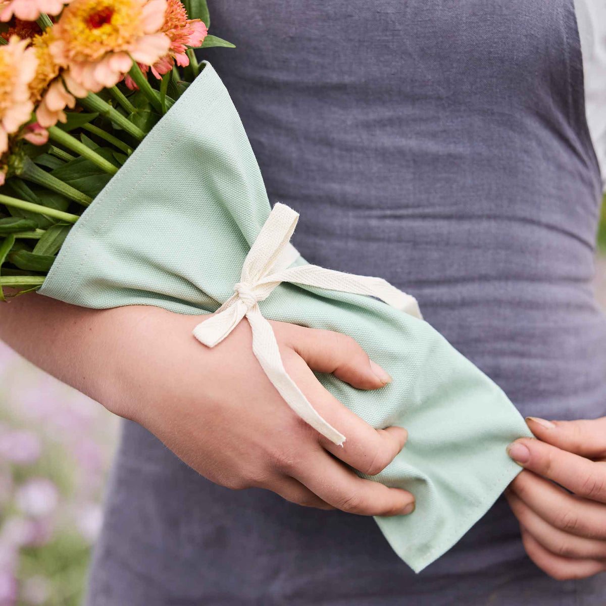 Person holding a bouquet of colorful flowers held together by boubqbags canvas bouquet sleeves in a natural setting