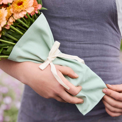 Person holding a bouquet of colorful flowers held together by boubqbags canvas bouquet sleeves in a natural setting
