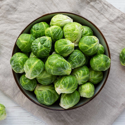 A bowl of several green Dagan F1 brussels sprouts showing layered leaves on a neutral cloth