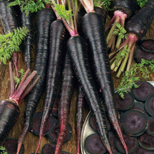 A group of black nebula carrots showing the nearly black skin with slices of the carrot surrounding it on a wooden surface.