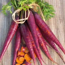 A bunch of cosmic purple carrots with green tops are lying on a wooden surface, ready for harvest.