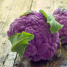 A head of richly purple cauliflower amethyst with leaves on the other edge on a wooden surface.