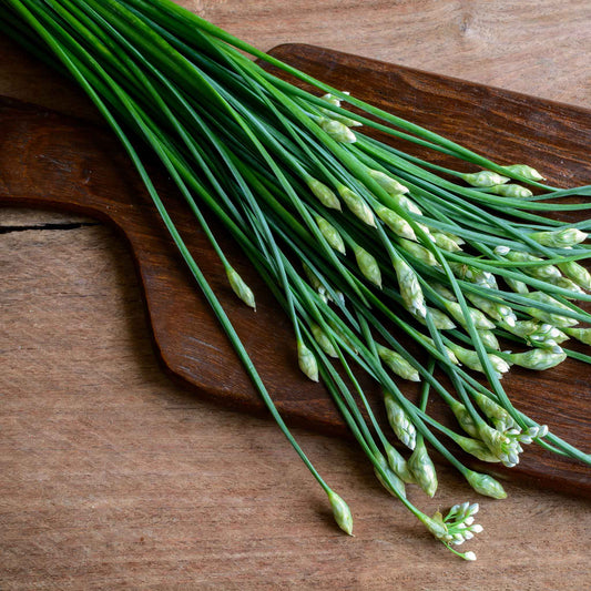 A close-up shot of green chive plants with slender, hollow leaves on a wooden cutting board.