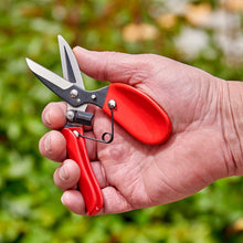 Hand holding a pair of red-handled comfortgel dead headers against a blurred green background