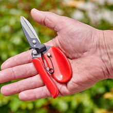 Hand holding a pair of red-handled comfortgel dead headers against a blurred green background