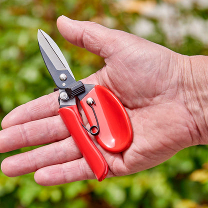 Hand holding a pair of red-handled comfortgel dead headers against a blurred green background