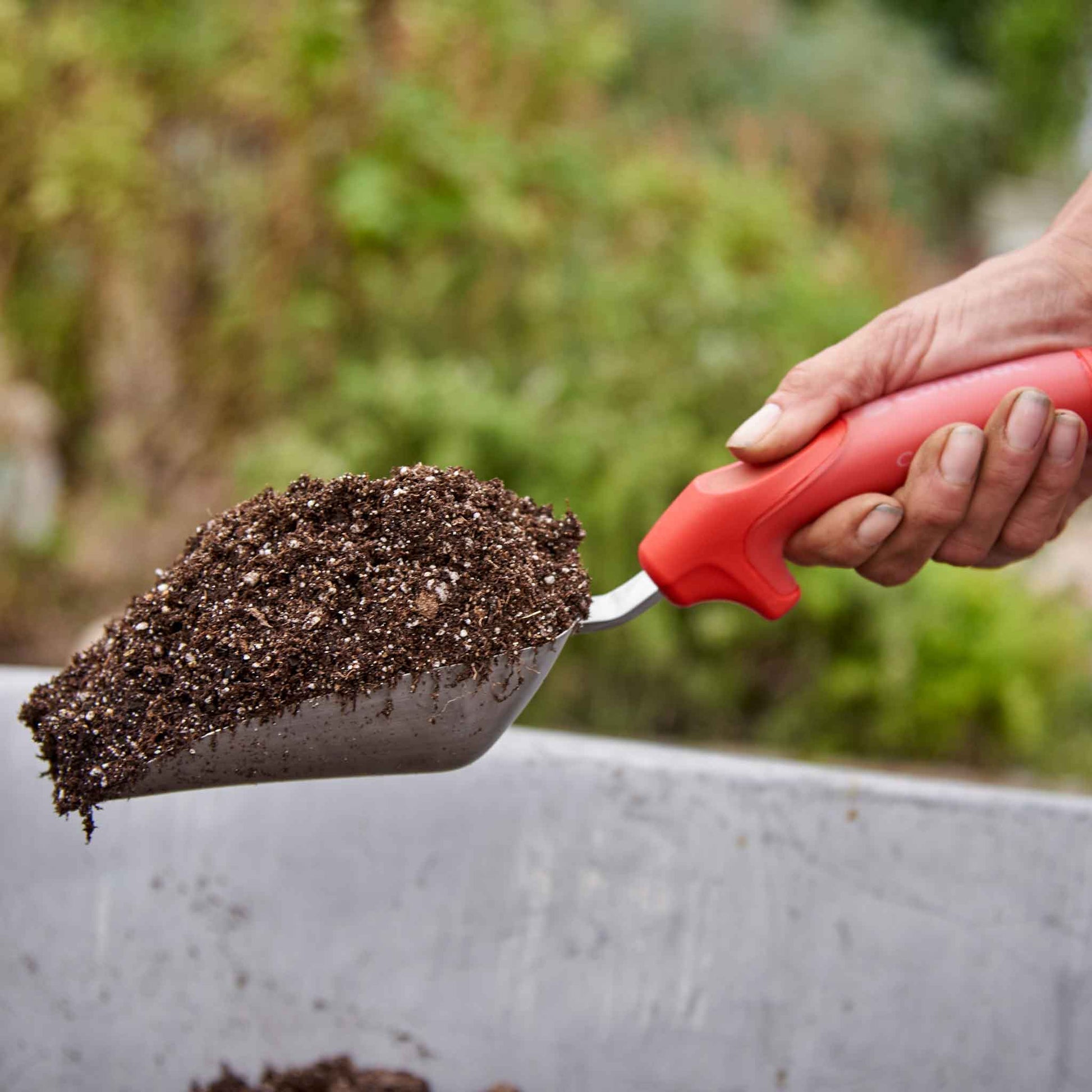 Person using a red handled corona comfortgel scoop to scoop soil with a blurred background
