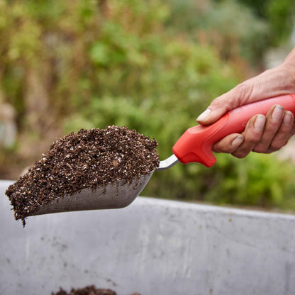 Person using a red handled corona comfortgel scoop to scoop soil with a blurred background