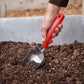 Person gardening with a red handled corona comfortgel scoop in a garden bed with soil.