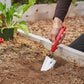 Hand using a red-handled corona comfortgel trow to dig into soil in a raised bed.