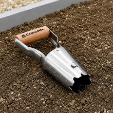 The corona classic wooden handle bulb planter with metal cone shaped digger laying on dirt in the garden