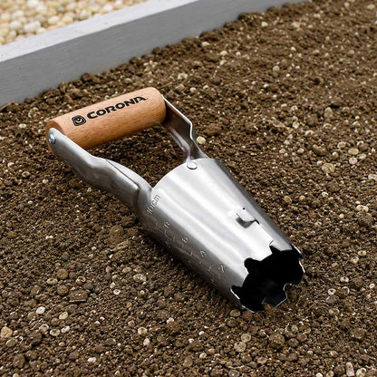 The corona classic wooden handle bulb planter with metal cone shaped digger laying on dirt in the garden