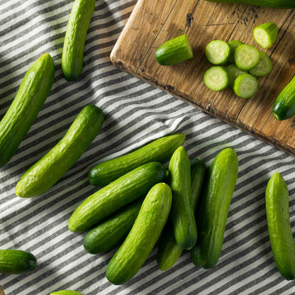 Mini me cucumbers on a striped cloth showing smooth skin, small size, and some slices showing the inside.